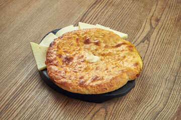 Delicious Georgian khachapuri - closed baked pie with homemade cheese on a wooden background