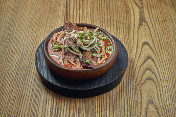 Yummy Lula Kebab in red sauce with onions in a ceramic bowl on a wooden background. Barbecued shish kebab from minced meat