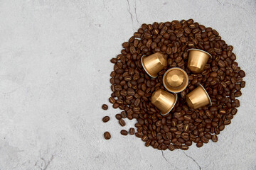 Caffeine, hot drinks and objects concept. Close up golden capsules or pods for coffee mashine with some roasted grains on gray concrete background. Top view with space for text. Selective Focus.