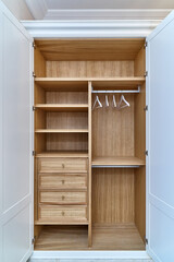 White wardrobe with wooden drawers and shelves. Wooden filling of wardrobe and white clothes hangers