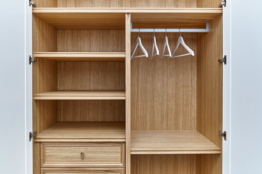White wardrobe with wooden drawers and shelves. Wooden filling of wardrobe and white clothes hangers