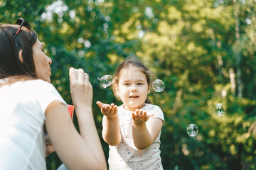 Fototapeta premium Cute toddler girl blows on soap bubbles with his mother in the sunny summer day