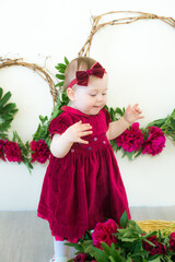 Little cute girl 1 year old in a dress of Marsala color with a wicker basket with peonies. Spring and flowers. Children's fashion
