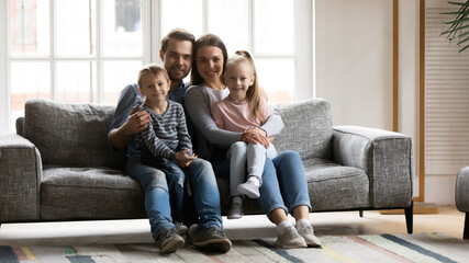 Family portrait cute adorable little kids sitting on mum and dad laps, looking at camera, smiling...