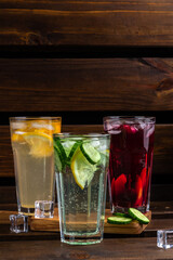 set of summer refreshing drinks on a wooden background with copy space. three glasses of red, yellow and green lemonade with ice cubes