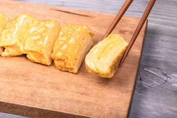 Tamago Japanese omelet on a wooden serving board and chopsticks hold a piece of omelet, close-up