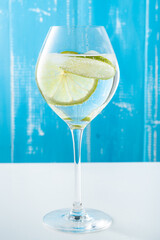 Cold summer delicious coctail with lime and ice in a glass with drops on the white and blue background.