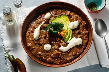 vegan chili soup without meat, with pinto beans and avocado, served with yogurt made from soy on linen tablecloths. healthy eating