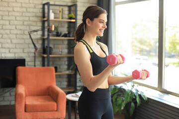 Fototapeta na wymiar Young beautiful sports girl in leggings and a top does exercises with dumbbells. Healthy lifestyle. A woman goes in for sports at home.