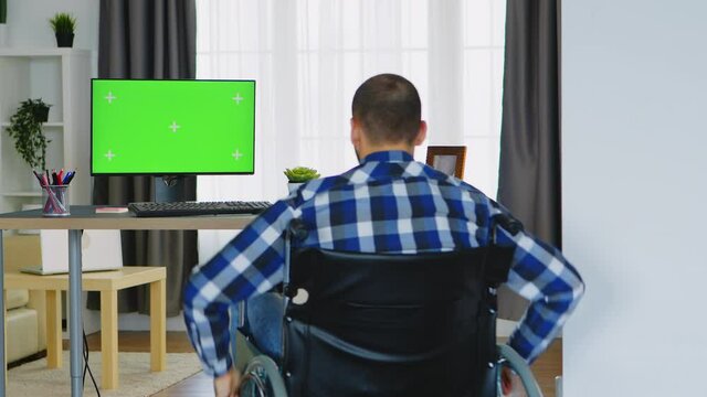 Businessman in wheelchair in front of computer with green screen. Handicapped invalid paralysed freelancer, immobilized entrepreneur working from home, ilness and disability