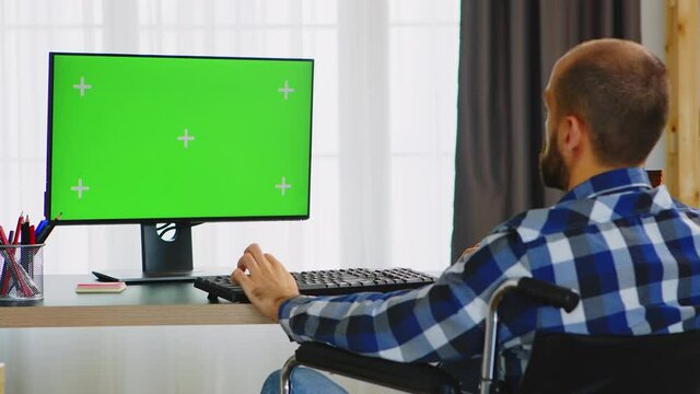 Invalid entrepreneur in wheelchair working on computer with green screen from home office. Handicapped invalid paralysed freelancer, immobilized entrepreneur working from home, ilness and disability