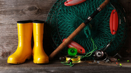 Fishing tackle and yellow rubber boots, flat lay on wooden vintage background
