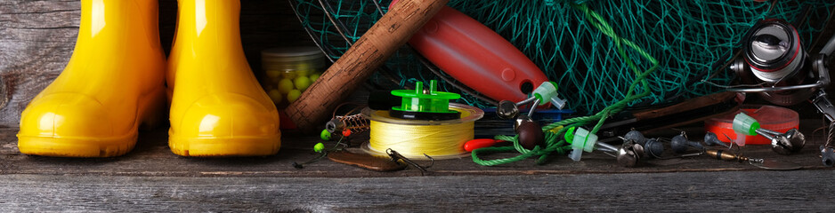 Fishing tackle and yellow rubber boots on a wooden vintage background