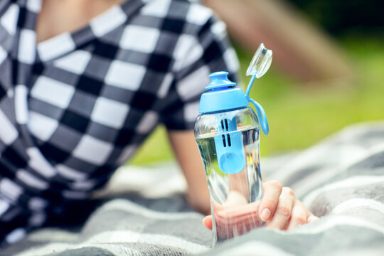 Woman holds the bottle of filtered water outdoors. Woman relaxes outdoors and holds the reusable bottle of fresh filtered water in hand.