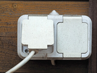 External electrical outlet on the wooden wall of the house. Plastic socket with protection from...