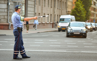 Police officer directing traffic in the city with police stick. Traffic police adjusts cars at the intersection of  avenue, rush hour. Policeman regulating traffic