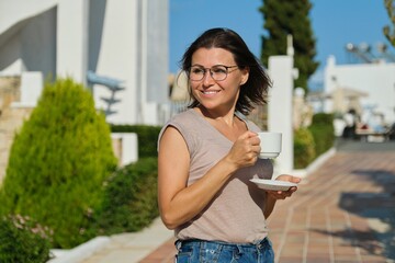 Mature woman in glasses with cup of coffee walking outdoor