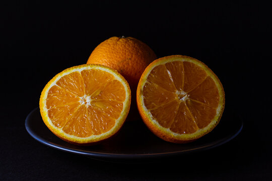 naranjas frescas cortadas en un plato negro sobre fondo negro