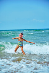 Happy little girl in mask for swimming running and jumping in the waves