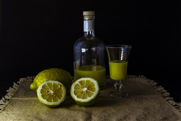 Obraz na płótnie Canvas limoncello licor de limón tradicional italiano con botella, copa y mitades de limón fresco