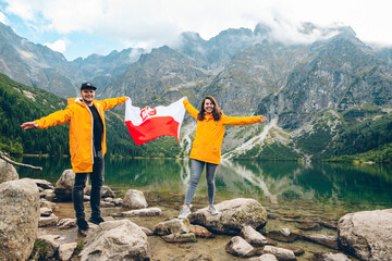 couple in yellow raincoats holding poland flag in front of lake in tatra mountains