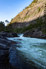 Obraz premium Waterfall in Norway with sun on a mountain in the background portrait