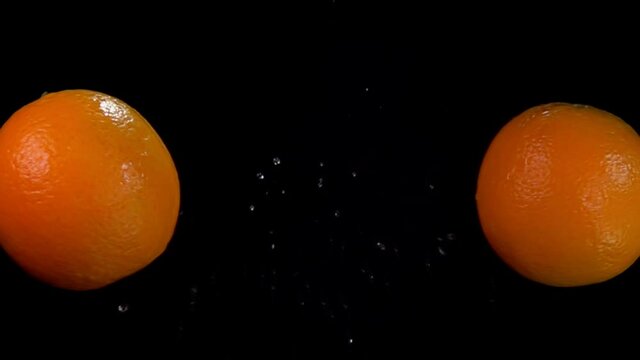 Two oranges are flying and colliding with each other rising splashes of water on the black background in slow motion