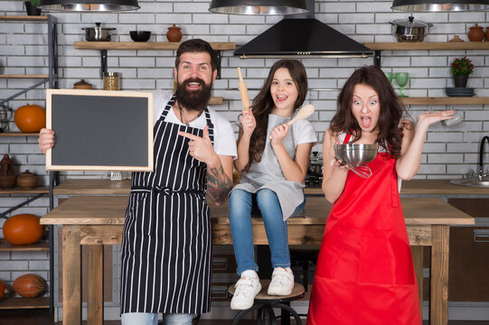 Mother And Father Teaching Daughter How To Cook. Small Girl With Mom And Dad In Kitchen. Do Everything Together. Cooking By Recipe. Fathers Day. Relatives Having Fun While Cooking