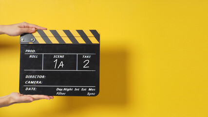 A Hand is holding Black clapperboard or movie slate on yellow background.It has written a number..