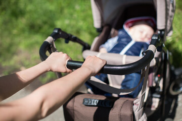 Obraz premium Young mother walking and pushing a stroller in the park