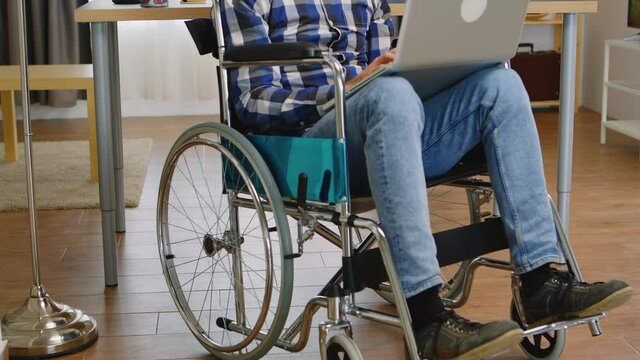 Handicapped businessman in wheelchair working on laptop in living room. Handicapped invalid paralysed freelancer, immobilized entrepreneur working from home, ilness and disability