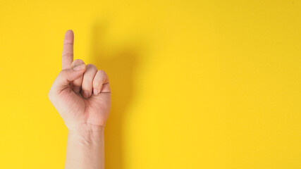 Male model is doing one finger or point up hand sign on yellow background. - obrazy, fototapety, plakaty