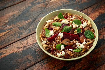 Buckwheat and beetroot salad with mushroom, walnut, spinach and feta cheese on rustic wooden table....