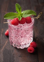 Glass with ice of cold summer pink lemonade cocktail with raspberries, mint and raw berries on wooden background.