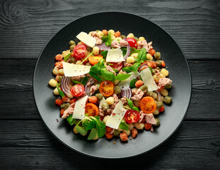 Mini potato gnocchi tricolour with tomato, spinach, Seasonal salad leaves and parmesan cheese on black plate