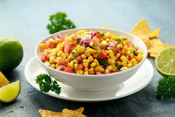 Mexican Corn Salsa in white bowl with lime and tortilla chips. Healthy food