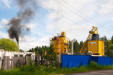 Fototapeta na wymiar yellow industrial plant for the production of asphalt and pipe with black smoke in the forest , the concept of environmental pollution