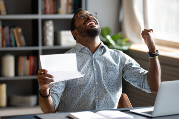 African businessman sit at workplace desk hold paper letter scream with joy got great business...