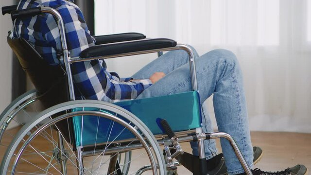 Invalid thoughtful man in wheelchair looking lost on window. Handicapped invalid paralysed person, alone at home, depression and health problems, pensive, sad and unhappy man