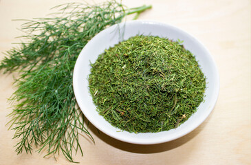 Green fresh dill and next to a plate of dried crushed. Natural seasoning, spice. All on a wooden...