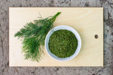 Green fresh dill and next to a plate of dried crushed. Natural seasoning, spice. All on a wooden chopping Board. Kitchen. Meal.