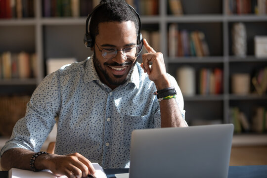 Focused African man sitting at desk wear headset watching webinar video course gain new knowledge use on-line application website. Manager talk to client provide professional help and support concept