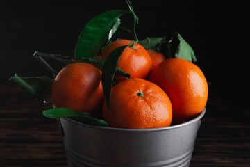 Fresh tangerines with leaves in a bucket on a wooden old background