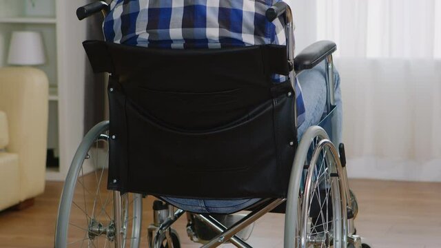 Sad paralyzed young man sitting in wheelchair. Handicapped invalid paralysed person, alone at home, depression and health problems, pensive, sad and unhappy man
