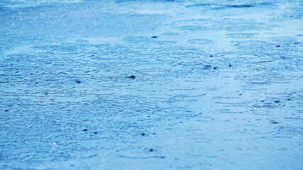 Puddle with raindrops and circles on the surface of the river water, background puddle rain