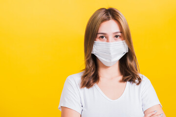Portrait Asian beautiful young woman stand crossed arm wearing face mask protection filter dust pm2.5 anti-pollution, anti-smog, air pollution and COVID virus on a yellow background, with copy space
