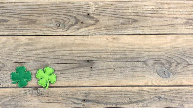 Female hand lays a border of felt four-leaf clover on old wooden background. Lucky shamrock, St.Patrick's day holiday symbol. Space for text, top view.