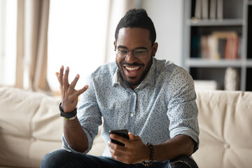 African man spend time at home use smartphone read sms feels excited scream with joy received...