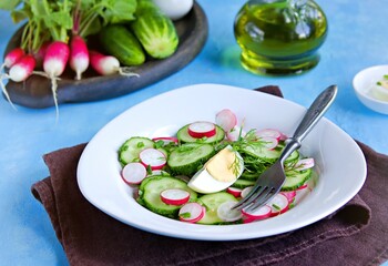 Summer salad with radish, cucumber and boiled egg in a white plate