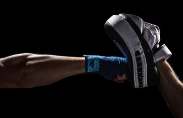 Boxing punch in to Punch Mitts. Training pad. Fighter athlete  wrapped hand is punching with fist and bare knuckles. Isolated on a black background. © ArmorProduction